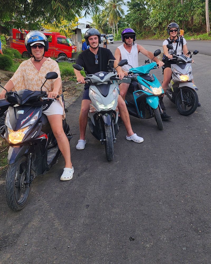 Four friends in helmets on rental scooters on a palm-fringed road