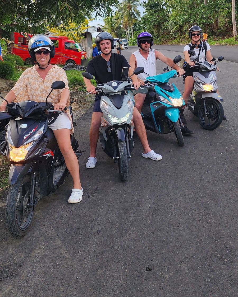 Four friends in helmets on rental scooters on a palm-fringed road