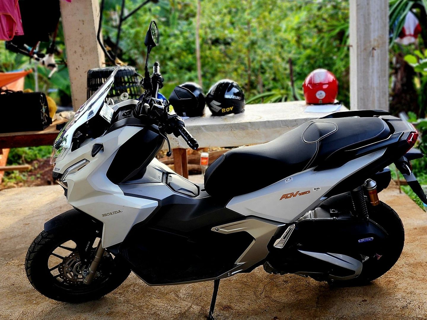 White Honda ADV 160 scooter parked under the rental shop shed, side view