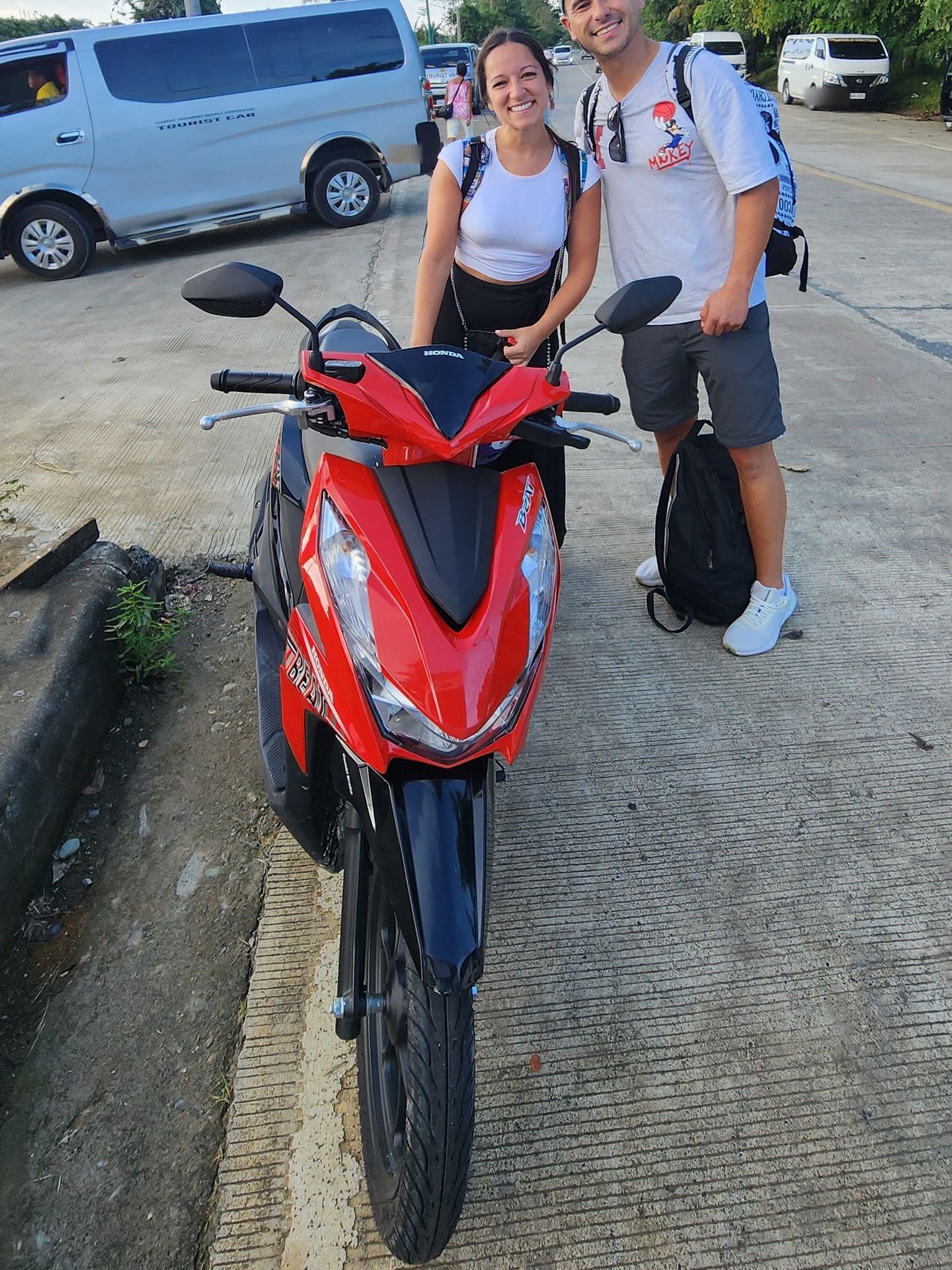 Red Honda BeAT scooter with a smiling couple near the airport