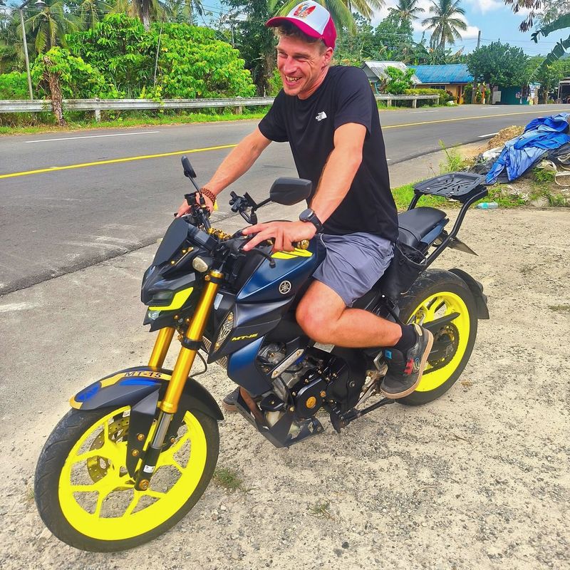Laughing rider on a Yamaha MT-15 with yellow wheels beside a palm-lined road